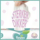 Hand trekt aan witte Pampers luier met de woorden 'STERKER DIKKER' in roze letters, tegen een achtergrond met zachte kleuraccenten en het Pampers-logo. Zijbalk geeft aan 'zacht & zacht reinigen', '0% parfum & alcohol', en 'plant-gebaseerd'.